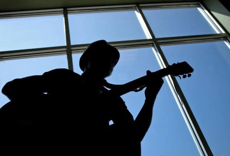 George Achini silhouetted against a window, playing guitar